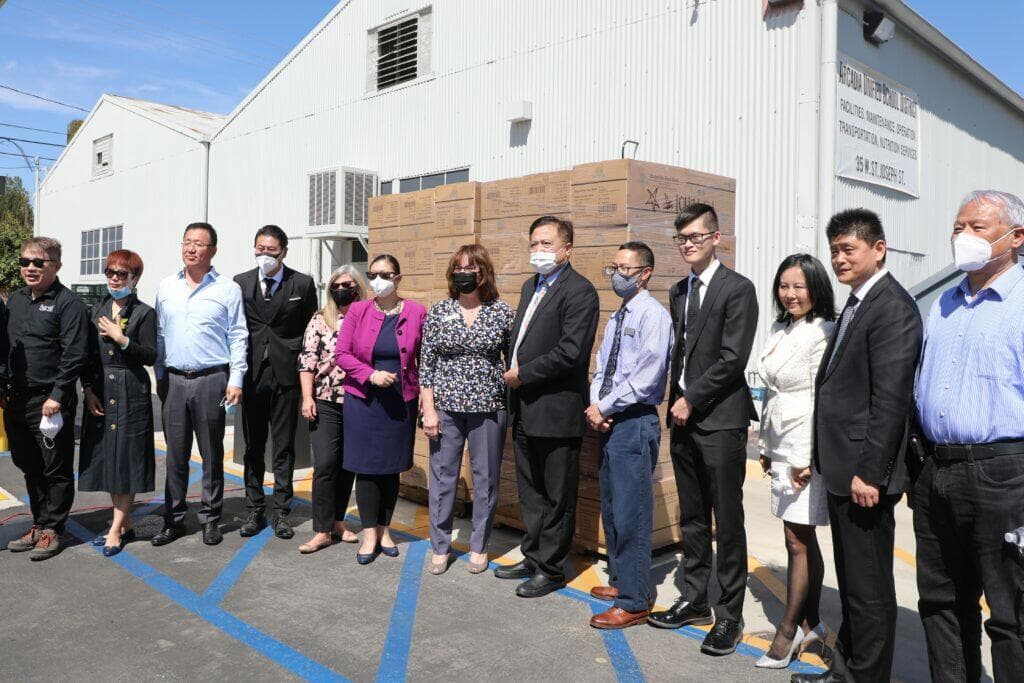社區僑界領袖與學區代表在捐贈的口罩物資前合影