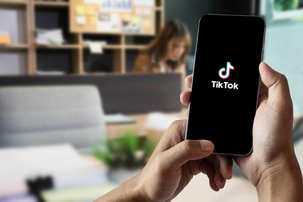 一隻手拿著顯示 TikTok 標誌的智慧型手機，背景是辦公室
