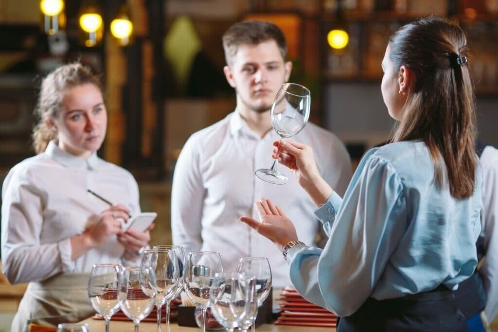講師手持酒杯,向兩名白襯衫服務生示範酒類服務要點