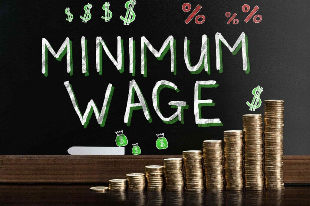 黑板上寫著 MINIMUM WAGE,旁邊是錢袋塗鴉與逐級升高的金幣堆